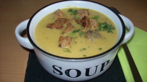 Eine cremige Kartoffelsuppe mit knusprigen Brotwürfeln in einer weißen Schüssel, auf einem dunklen Untersetzer serviert.
