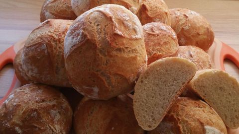 Krosse Weizenbrötchen liegen auf einem Holzbrett, während ein Adventskranz im Hintergrund stimmungsvoll leuchtet.