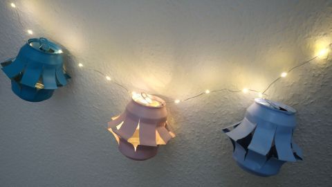 Bunte Lampionkette aus Getränkedosen hängt an einer Wand, beleuchtet mit warmen Lichtern für festliche Atmosphäre.