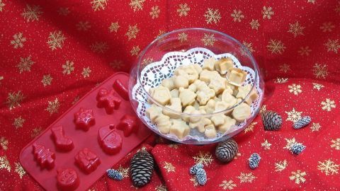 Eine Schale mit Karamellpralinen steht auf einem festlichen roten Hintergrund, umgeben von Weihnachtsdekoration.