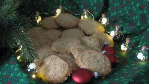 Auf einem festlich geschmückten Tisch liegen goldene Kekse, umgeben von Dekorationen und Lichtern, ideal für winterliche Anlässe.