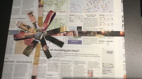 Geschenkpapier aus Zeitung ist kreativ verpackt, mit bunten Bändern dekoriert und liegt auf einem dunklen Untergrund.