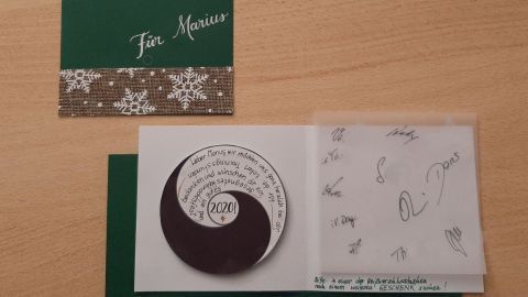 Eine grüne Weihnachtskarte mit Yin und Yang Symbol liegt offen auf einem Holztisch, umgeben von einer grünen Umschlagklappe.