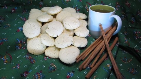 Weiße Schmalzwölkchen liegen auf einem grünen Tuch neben einer Tasse Ingwer-Zimt-Tee und Zimtstangen.