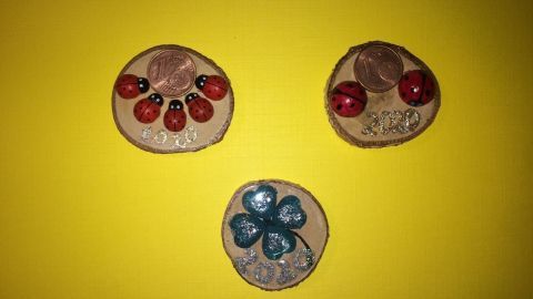 Drei handgemachte Magnete mit bunten Dekorationen liegen auf einem gelben Hintergrund bereit zum Basteln für den Jahreswechsel.