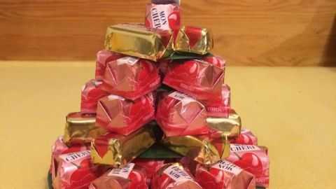 Ein Mini-Weihnachtsbaum aus Pralinen steht auf einem Teller, farbenfrohe Süßigkeiten bilden die Baumstruktur in festlicher Umgebung.