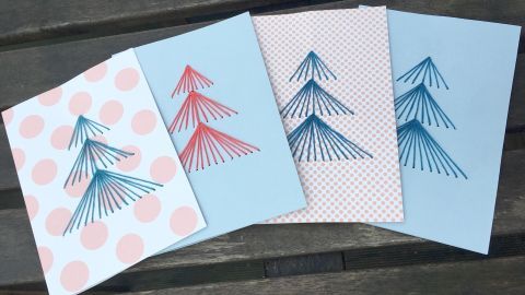 Bunt gestaltete Weihnachtskarten mit gestickten Tannenbäumen liegen auf einem Holztisch und strahlen festliche Stimmung aus.