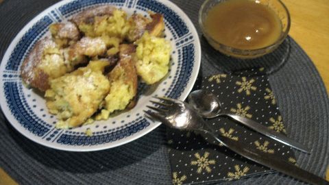 Ein Teller Kartoffelschmarrn liegt auf einem Tisch, neben einer Schüssel mit Sauce, umgeben von Besteck.