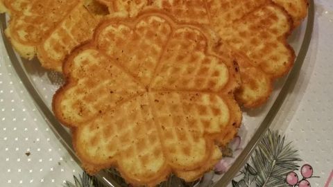 Knusprige Eierlikör-Waffeln liegen auf einem herzförmigen Teller, umgeben von festlicher Dekoration und Licht.