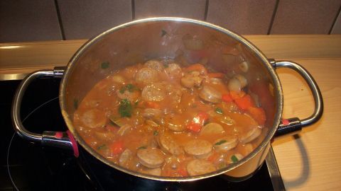 Ein dampfender Topf mit Bratwurst-Ragout und buntem Paprika kocht auf einem Herd in einer modernen Küche.