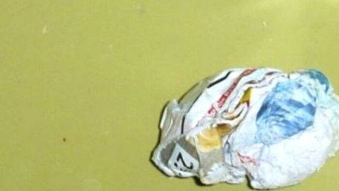 Ein zusammengeknülltes Papierstück liegt neben einem glänzenden Abfluss in einer gelben Umgebung, was auf das Vernichten von Adressen hindeutet.