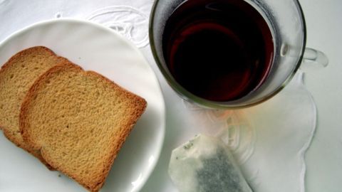 Ein Glas schwarzer Tee steht neben zwei Scheiben Brot auf einem weißen Untergrund, ideal zur Linderung von Durchfall.