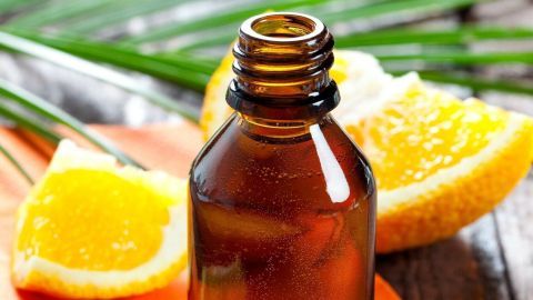 Ein braunes Fläschchen mit Orangenöl steht auf einem orangefarbenen Tuch, umgeben von frischen Orangenscheiben und grünem Gras.