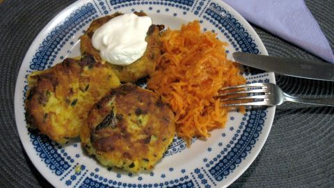 Kartoffel-Rösti-Taler liegen auf einem Teller, garniert mit Sauerrahm und begleitet von geraspelten Karotten.