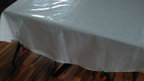 Eine Tischdecke aus Stoff schützt den Tisch vor Flecken und steht auf einem Holzfußboden. Die Oberfläche glänzt leicht.