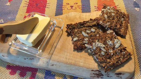Knäckebrot liegt auf einem Holzbrett, während eine Butterklinge Butter daneben bereitstellt, um das Brot zu genießen.