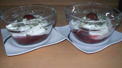 Zwei Pflaumen-Joghurt-Becher stehen auf weißen Tellern, gefüllt mit Joghurt und Pflaumenkompott, in einer hellen Umgebung.