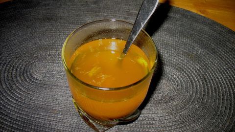 Ein Glas Kurkuma-Ingwer-Tee mit Zitrone steht auf einem runden Tischset, begleitet von einem Löffel, in angenehmer Beleuchtung.
