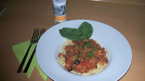 Ein Teller mit Thunfisch-Tomaten-Salsa, garniert mit frischen Blättern, steht auf einem Tisch mit Besteck.