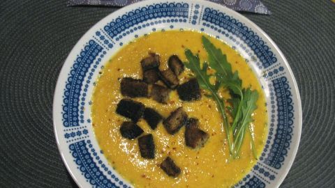 Eine Karotten-Creme-Suppe mit Orange und Ingwer wird in einer schönen Schüssel serviert, garniert mit leichten Kräutern.