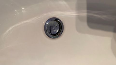 Ein Abflussloch in einer Badewanne zeigt sich in der Nähe von glattem, weißem Material, das Wasser abführen soll.