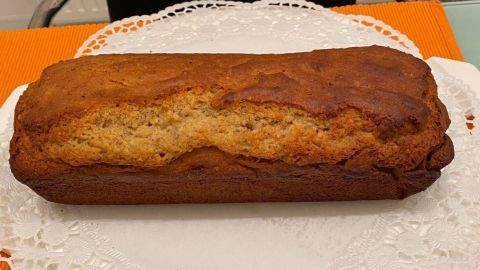 Ein Nuss-Marzipan-Kuchen liegt auf einer Spitze serviert, umgeben von einem weißen Tischtuch und orangefarbenem Hintergrund.