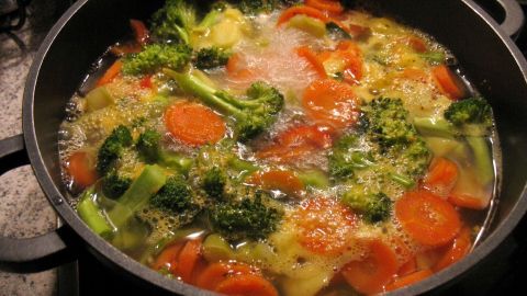 In einem schwarzen Topf kocht eine bunte Gemüsesuppe mit broccoli und Karotten auf dem Herd.