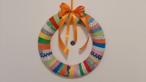 Ein bunter Türkranz aus Stoffresten hängt an einer Wand, geschmückt mit einer orangefarbenen Schleife und Musterstoffen.