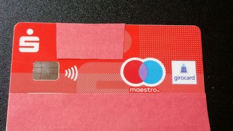 Eine rote Bankkarte liegt auf einer dunklen Oberfläche, bereit für kontaktloses Bezahlen und das sichere Verstecken der Geheimzahl.