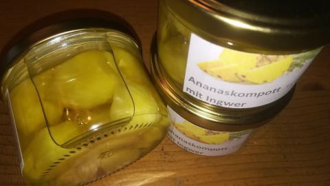 Kleine Gläser mit Ananaskompott und Ingwer stehen auf einer Holzoberfläche, gefüllt mit leuchtend gelben Fruchtstücken.