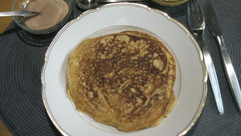 Ein Pfannkuchen liegt auf einem weißen Teller, umgeben von Besteck und kleinen Schüsseln mit Dips auf einem Platz.