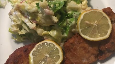 Zwei paniertes Schweinefilets liegen auf einem Teller, garniert mit Zitronenscheiben, neben einem frischen Schlaat.