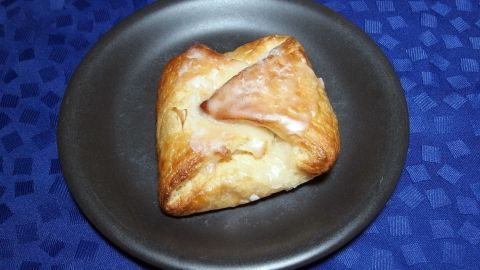 Eine Quarktasche mit Apfel liegt auf einem schwarzen Teller, umgeben von blauer Tischdecke, appetitlich und golden gebacken.