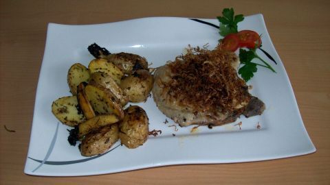 Auf einem weißen Teller liegt ein saftiges Schweinekotelett, bedeckt mit knusprigem, frittiertem Sauerkraut, neben goldbraunem Gemüse.
