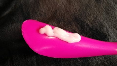 Ein pinker Ausstrichhilfe ist mit Lotion gefüllt und liegt auf einem dunklen Tuch, bereit für das Eincremen des Rückens.