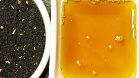 Schwarzkümmelöl in einem flachen Behälter neben schwarzen Kümmelsamen, bereit zur Anwendung für die Fußpflege.