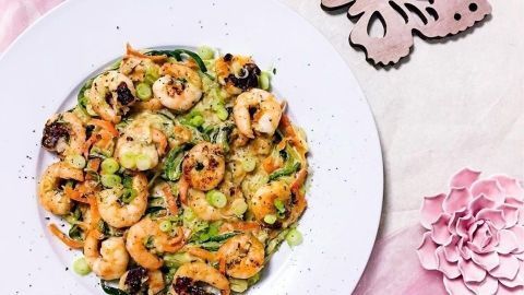 Cremige Zoodles mit Garnelen liegen appetitlich auf einem weißen Teller, umgeben von dekorativen Blumen und Schmetterlingen.