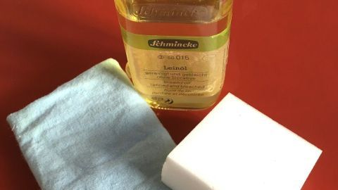 Ein Fläschchen Reinigungsmittel steht neben einem Schwamm und zwei Reinigungstüchern, bereit zum Linoleum reinigen.