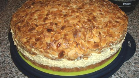 Ein rundes Bienenstich mit Biskuitteig, bedeckt von goldbraunen, gerösteten Mandeln, steht auf einer Platte.