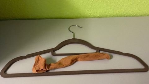 Ein flacher Kleiderbügel mit einem Nylonstrumpf liegt auf einer Tischplatte. Der Hintergrund ist grün gestrichen.