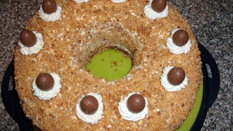 Ein runder Frankfurter Kranz ist mit Sahne und Schokoladeneiern dekoriert und auf einem grünen Teller platziert.