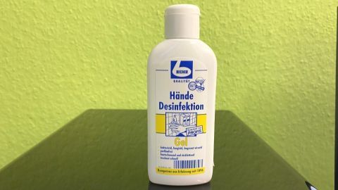 Eine Flasche mit Desinfektionsmittel steht auf einem Tisch vor einer grünen Wand und zeigt die Aufschrift "Hände Desinfektionsmittel".