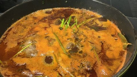 In einem grünen Topf köcheln zarte Ochsenbäckchen in einer aromatischen Rotweinsoße auf der Herdplatte.