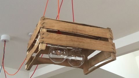 Ein Lampenschirm aus einer Obstkiste hängt von der Decke und beleuchtet den Raum mit warmem Licht.