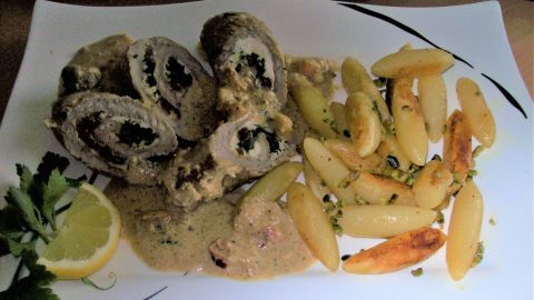 Kalbs-Involtini liegen auf einem Teller mit Schupfnudeln und einer hellen Soße, garniert mit Zitrone und Petersilie.