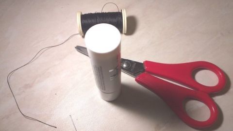 Ein rotes Scherenset liegt neben einer Nähspule und einer Kleberolle auf einem hellen Untergrund, während der Faden vorbereitet wird.