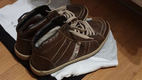 Zwei Winterschuhe liegen auf einem alten Pullover als Ablage in einem Raum mit Fußboden aus Holz.