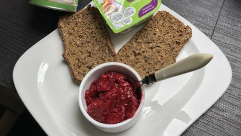 Auf einem weißen Teller liegt zwei Scheiben Low-Carb-Brot, daneben ein Schälchen mit roter Marmelade und Aufstrichen.