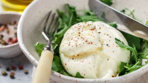 Eine cremige Burrata liegt auf einem Bett aus frischem Rucola, zusammen mit Gewürzen, die bereit für die Zubereitung sind.