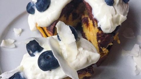 Ein Choco-Vanilla-Apfelkuchen ist auf einem Teller angerichtet, garniert mit Sahne, Blaubeeren und Kokosflocken.